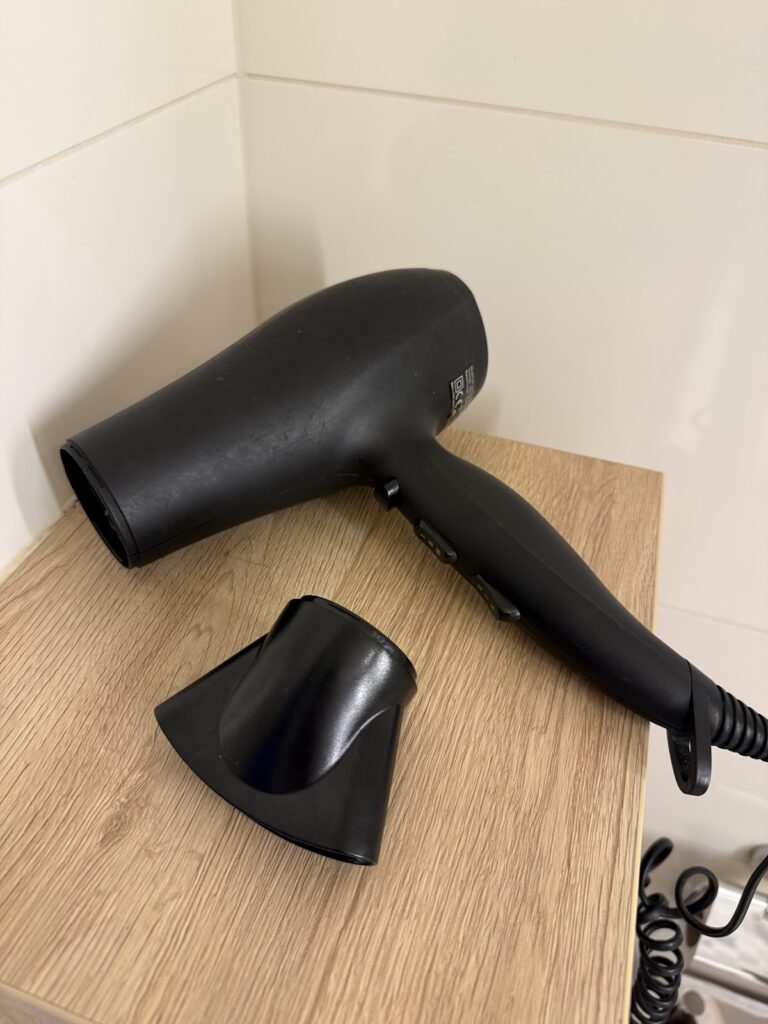 Black hotel hairdryer on wooden bathroom shelf