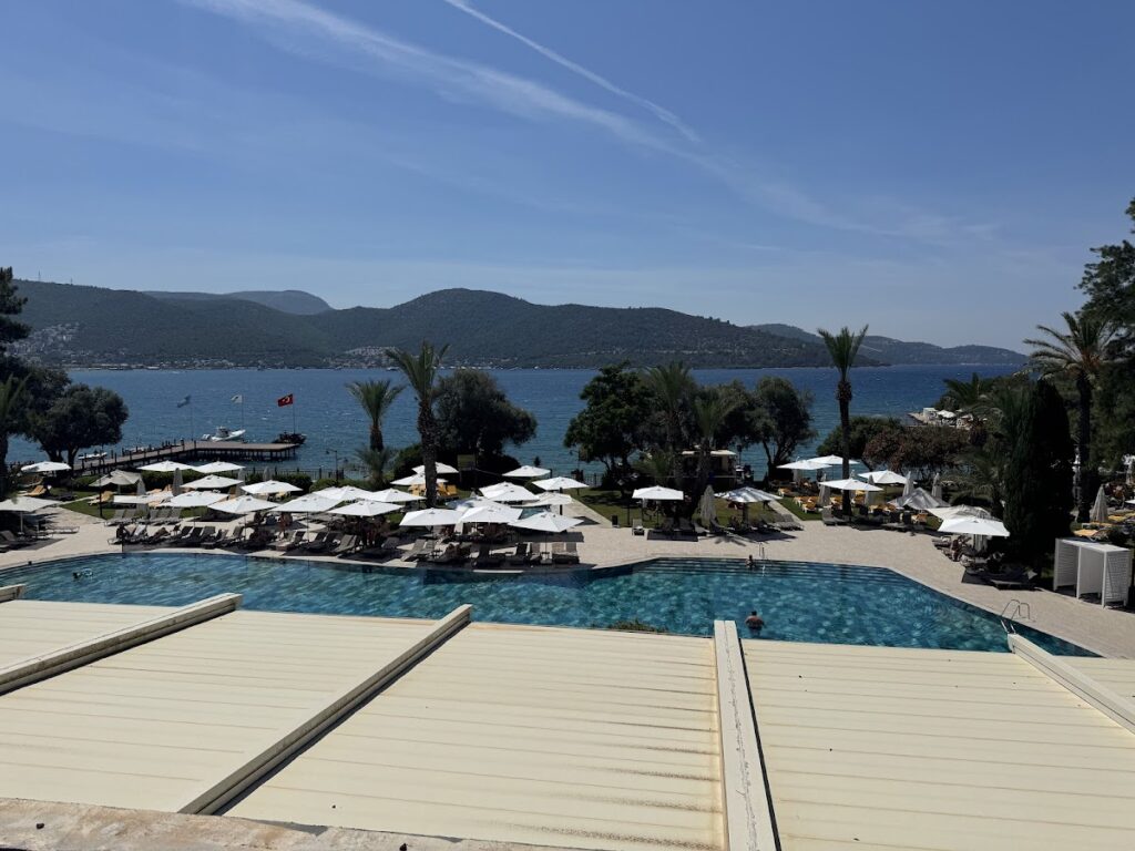 Oceanfront pool with umbrellas, mountains, and anchored boats