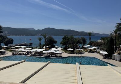 Oceanfront pool with umbrellas, mountains, and anchored boats