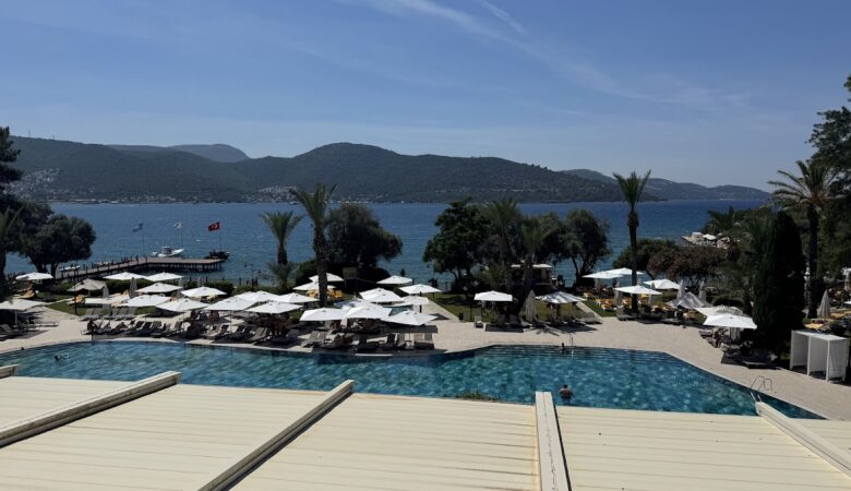 Oceanfront pool with umbrellas, mountains, and anchored boats