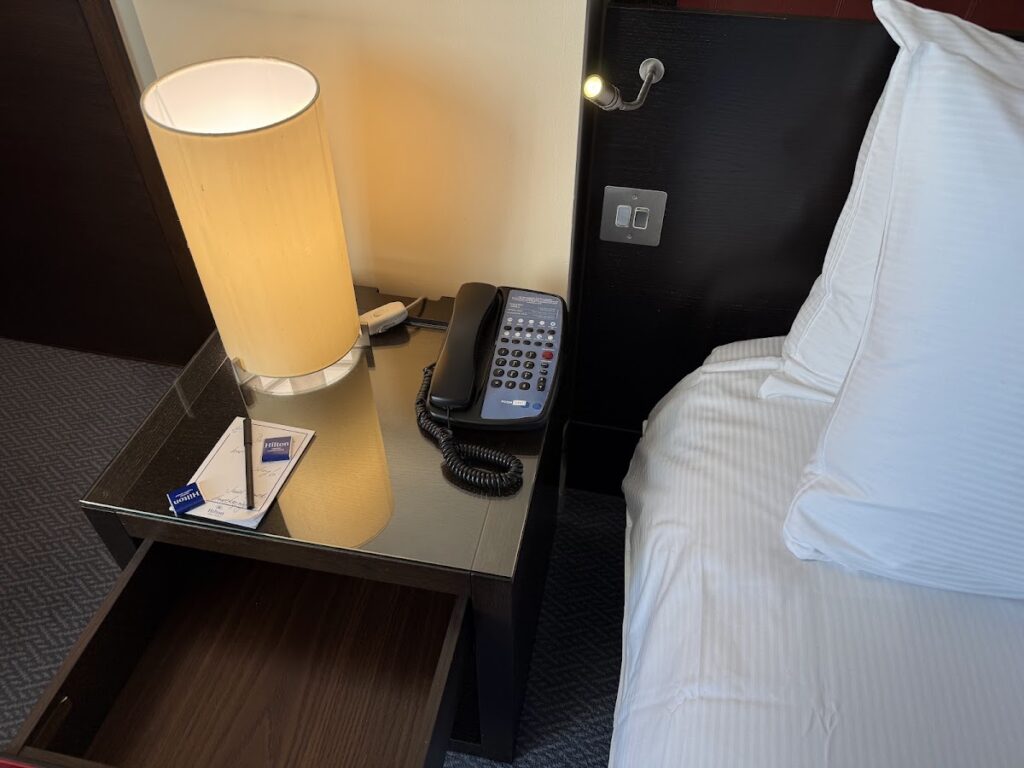 Bedside table with lamp and phone at Hilton Canary Wharf