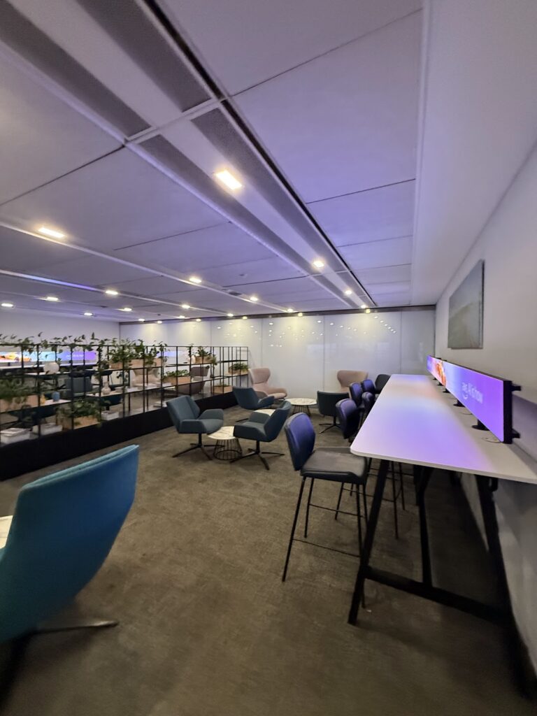 Modern airport lounge with seating, screens, and views.