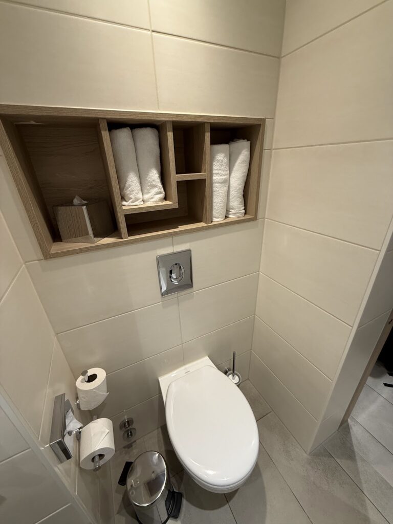 Clean bathroom with toilet, shelving, and towel storage